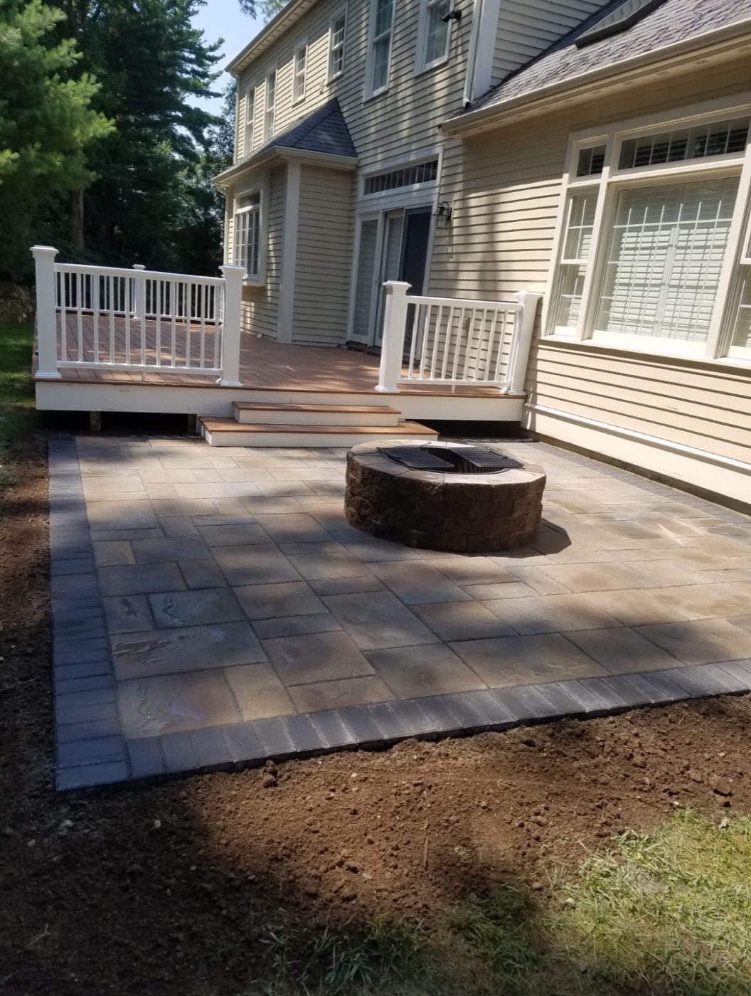 Paver patio with fire pit below a deck